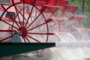 close up of red paddlewheel boat on a river with water spray