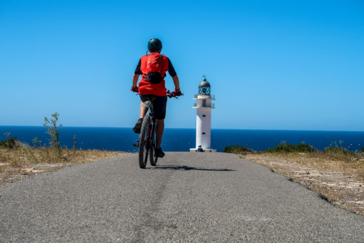 A boy riding the bicycle towards the lighthouse on Formentera