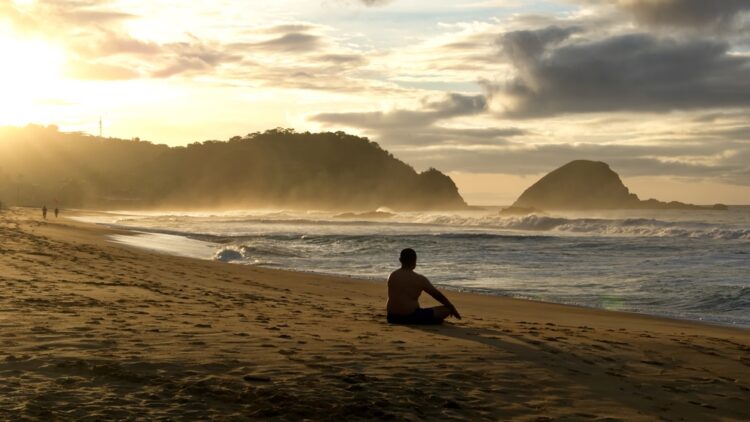 Man sitting on the beach at sunrise at Zipolite, Mexico