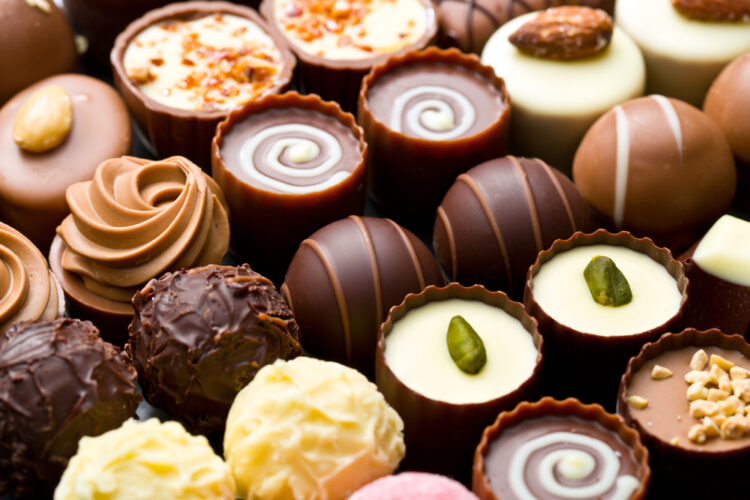 Assorted gourmet chocolates close-up, perfect treats to explore on your culinary travels. Discover luxury in white, milk, and dark chocolate variety with nuts and artistic swirls on a travel guide indulgent sweets page.
