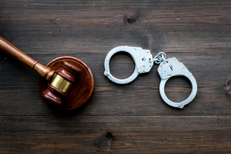 Alt text: "Wooden gavel and metal handcuffs on a rustic dark wood background representing legal authority and law enforcement for an article on travel safety and legal awareness." This descriptive alt text is tailored to be relevant for a travel guide website that might