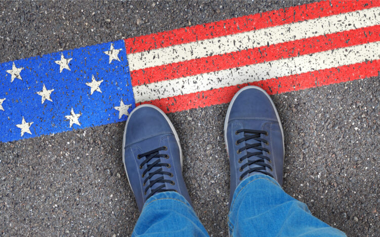 Alt text: "Traveler's perspective of feet in blue sneakers standing on an American flag-themed crosswalk, symbolizing exploration and patriotism in the USA."