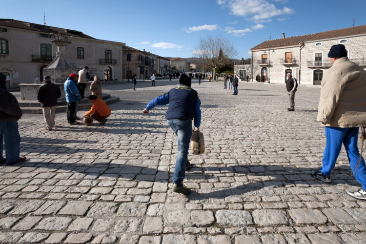 "Visitors enjoying a sunny day on the cobblestone square of a historic European town with traditional stone buildings and a clear blue sky."