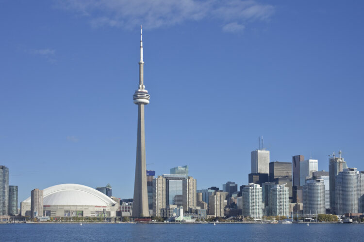 Alt text: "Iconic Toronto skyline with CN Tower dominating the scene, set against a clear blue sky, with the Rogers Centre and bustling waterfront - perfect for exploring urban sights in Canada."