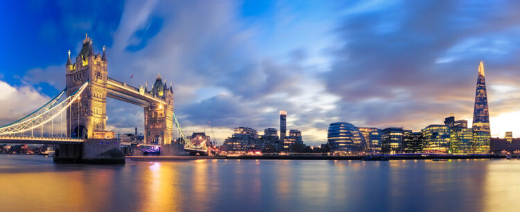 Alt text: "Breathtaking panoramic view of the iconic Tower Bridge and the modern Shard skyscraper during twilight in London, with glowing city lights reflecting in the Thames River."