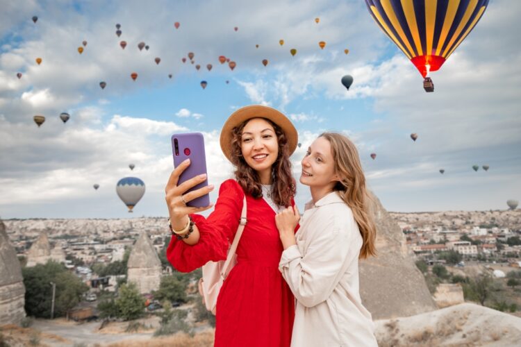 Two female friends taking selfies in front of air balloons in the sky