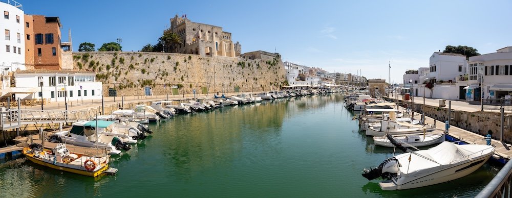 Mahón Harbor in Menorca, with boats docked on both sides and the fortress