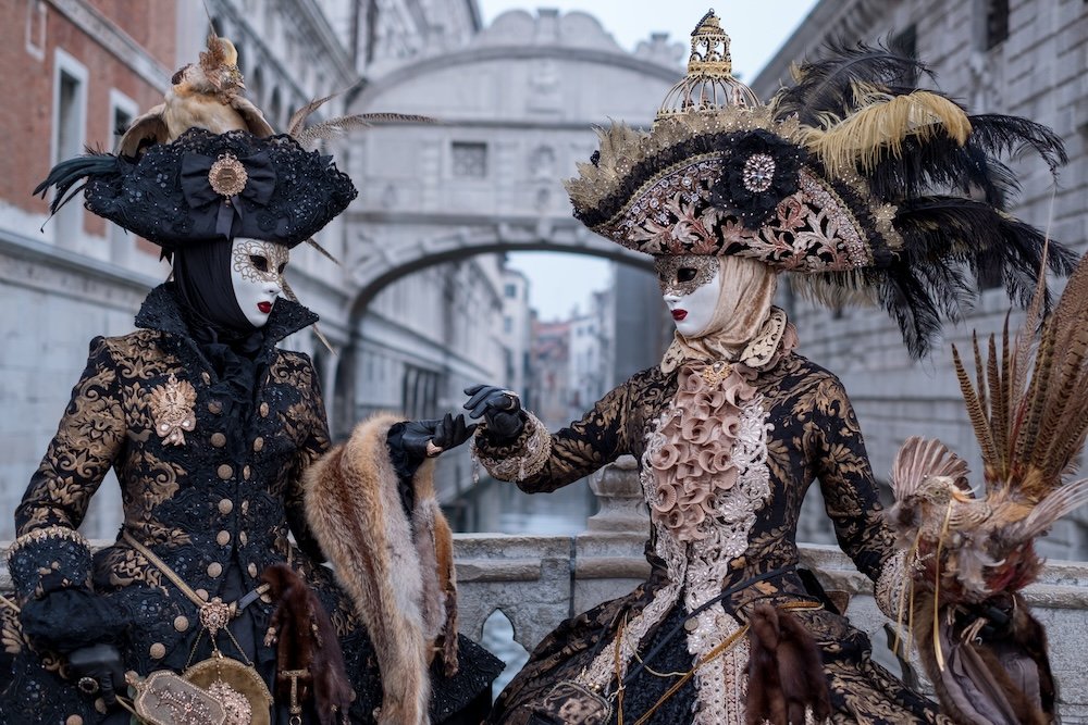 Two woman in costumes and masks, carrying feathered bird and birdcage