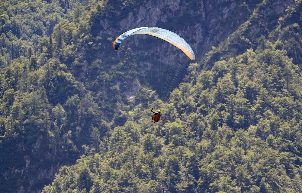 Colorful paraglider descending over the green alpine landscape of Lake Bohinj and Triglav National Park in Slovenia