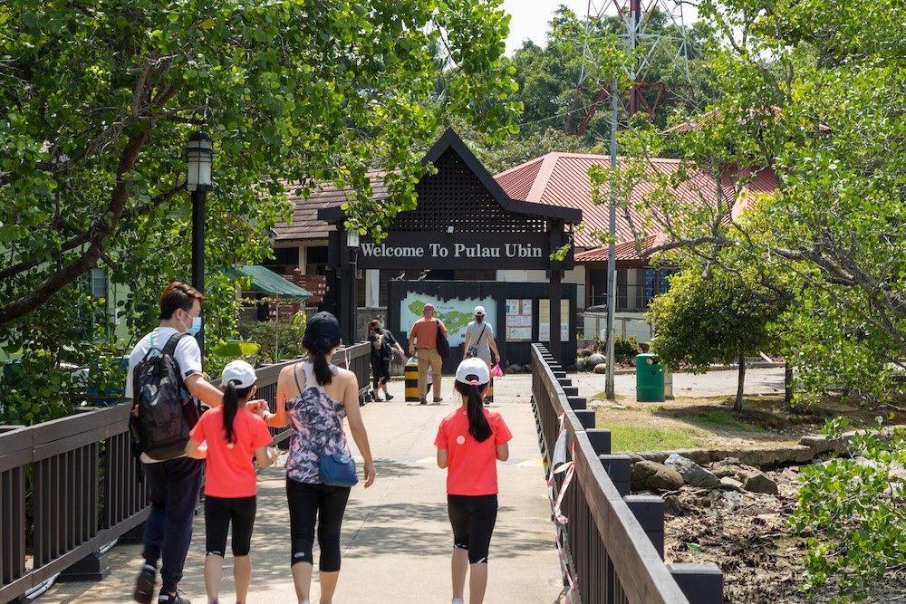 A family visits Pulau Ubin in Singapore, walking towards the entrance surrounded by lush greenery and scenic outdoor setting of the island